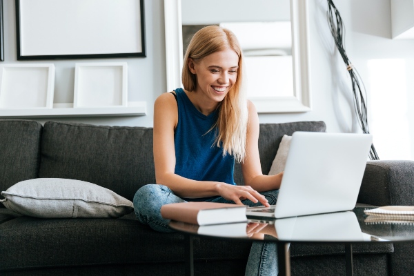 Happy pretty young woman sitting on sofa and using laptop at home